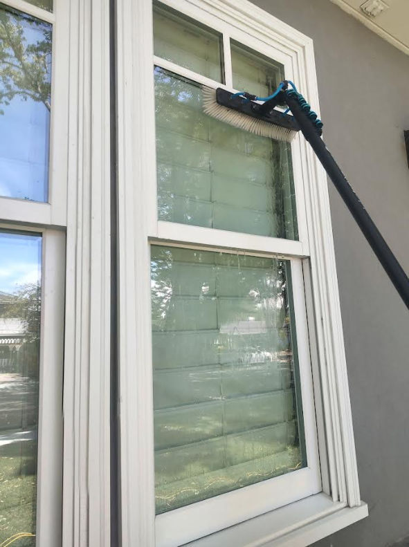 Water-fed brush on an extendable pole cleaning an exterior window pane